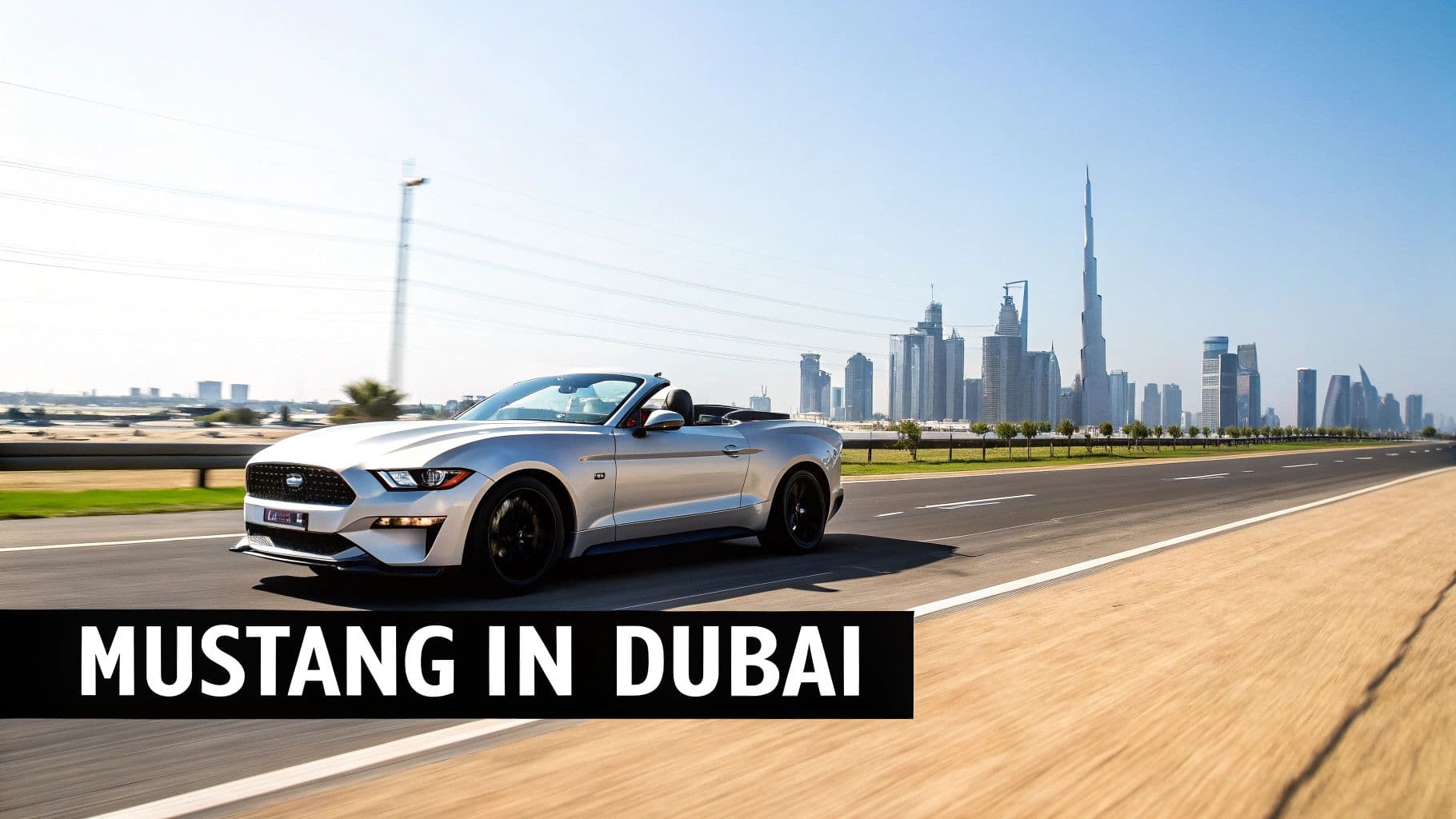 A silver Ford Mustang convertible drives on a road in Dubai with the city skyline and Burj Khalifa in the background.
